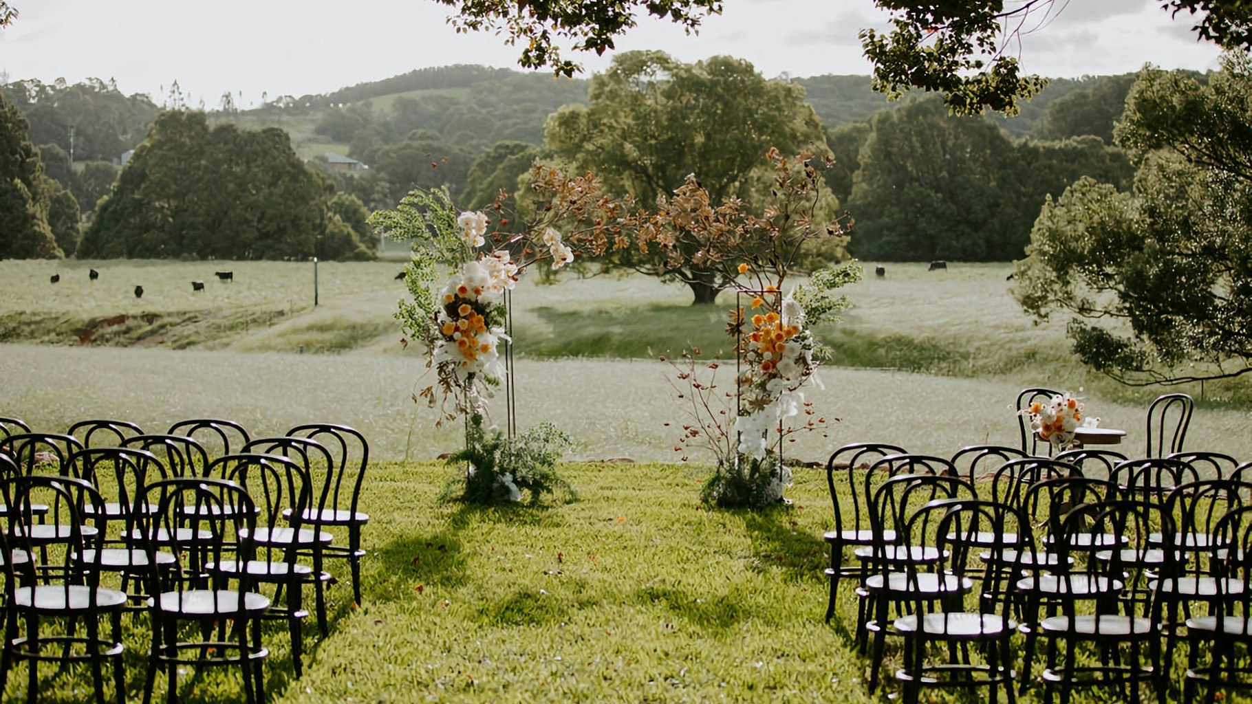 Outdoor wedding ceremony in green fields, with a floral arbour.